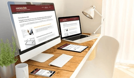 Fotografia modificata graficamente di una scrivania d'ufficio con alcuni device (un PC fisso, un notebook, un tablet e uno smartphone) sui cui schermi è visibile la home page di questo sito web: carrerailab.it
